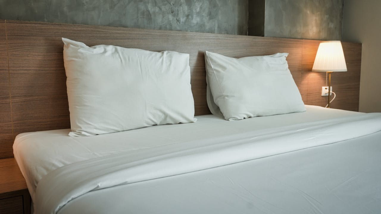 A clean and contemporary hotel room featuring minimalist bedding and a warm bedside lamp.