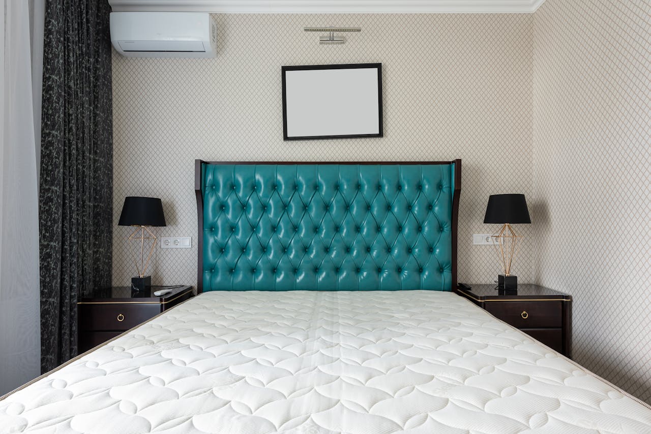 Mattress on bed with upholstery between lamps on bedside tables under air conditioning in house