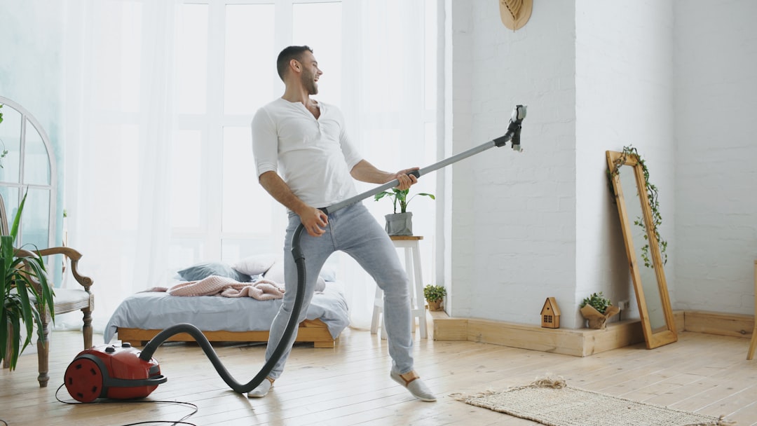 Dancing young man having fun cleaning house with vacuum cleaner at home