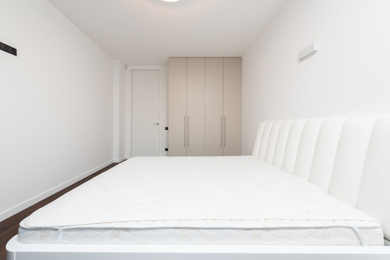 Contemporary minimalist bedroom featuring a white mattress and sleek wardrobe under soft lighting.